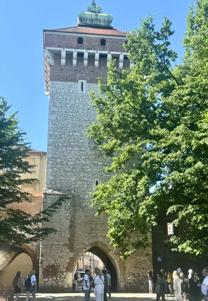"Florian Gate viewed from Planty Park, a medieval brick tower framed by lush trees and a pedestrian pathway.