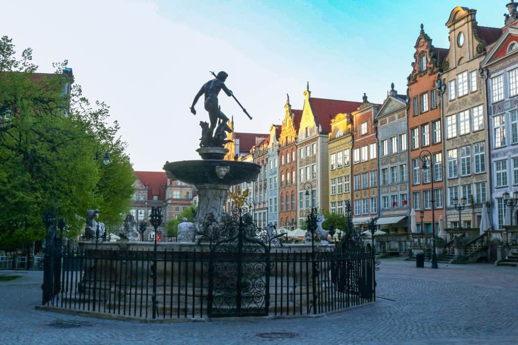 Statue of Neptune holding a trident atop the ornate Neptune Fountain in Gdańsk, Poland, surrounded by colorful facades and cobblestone streets