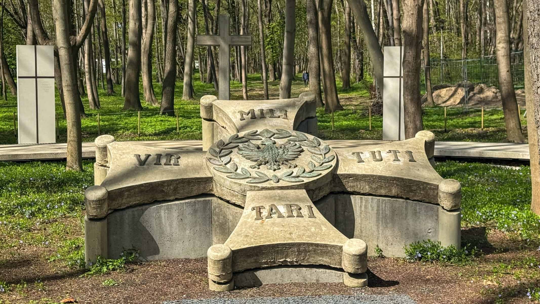 Stone memorial cross in a wooded area at Westerplatte. A circular emblem sits at the center, featuring the Polish Eagle. The monument stands quietly among trees, evoking remembrance and reflection.
