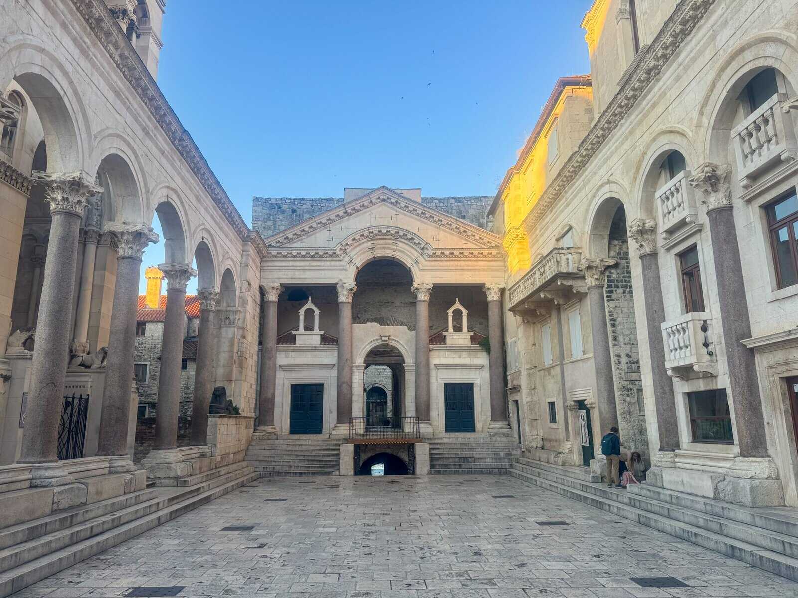 Stone courtyard inside Diocletian’s Palace in Split, Croatia, featuring classical columns, arches, and statues around a central temple-like structure under soft early-evening light.