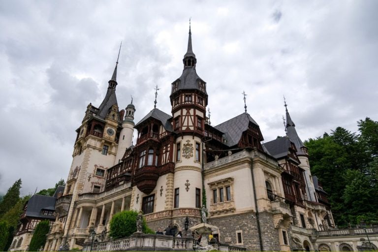 Peleș Castle in Sinaia, Romania, with ornate towers and timber-framed architecture set against forested hills.
