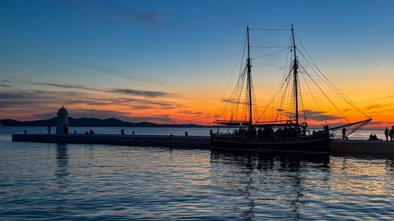Traditional sailing boat silhouetted against an orange sunset on Zadar’s waterfront in Croatia.