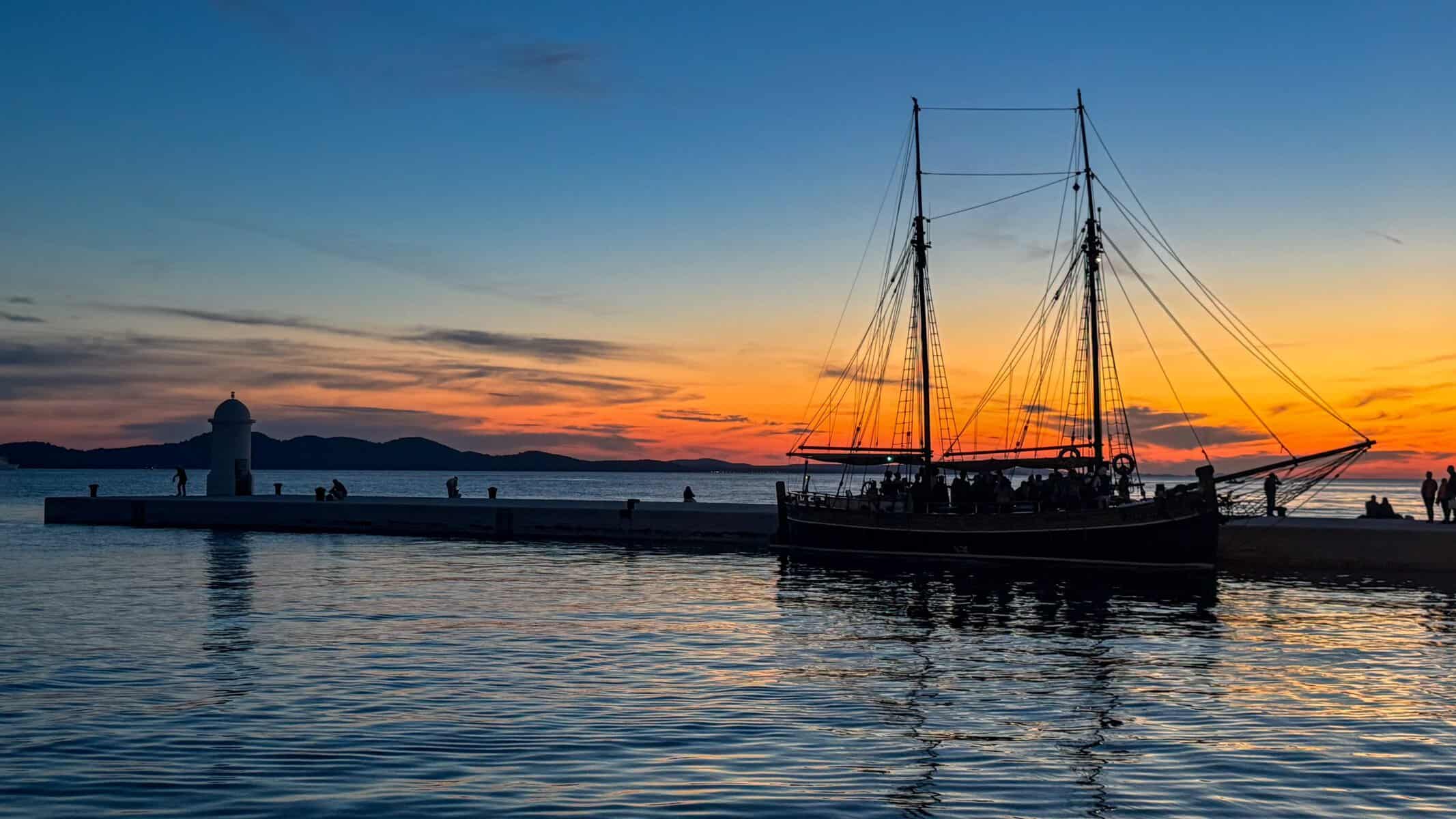 Traditional sailing boat silhouetted against an orange sunset on Zadar’s waterfront in Croatia.